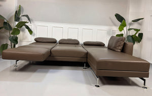 Gebrauchtes braunes Brühl Moule Designer Leder Sofa vor einer Wand, stilvoll und modern eingerichtet.