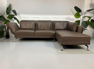 Gebrauchtes braunes Brühl Moule Designer Leder Sofa vor einer Wand, stilvoll und modern eingerichtet.