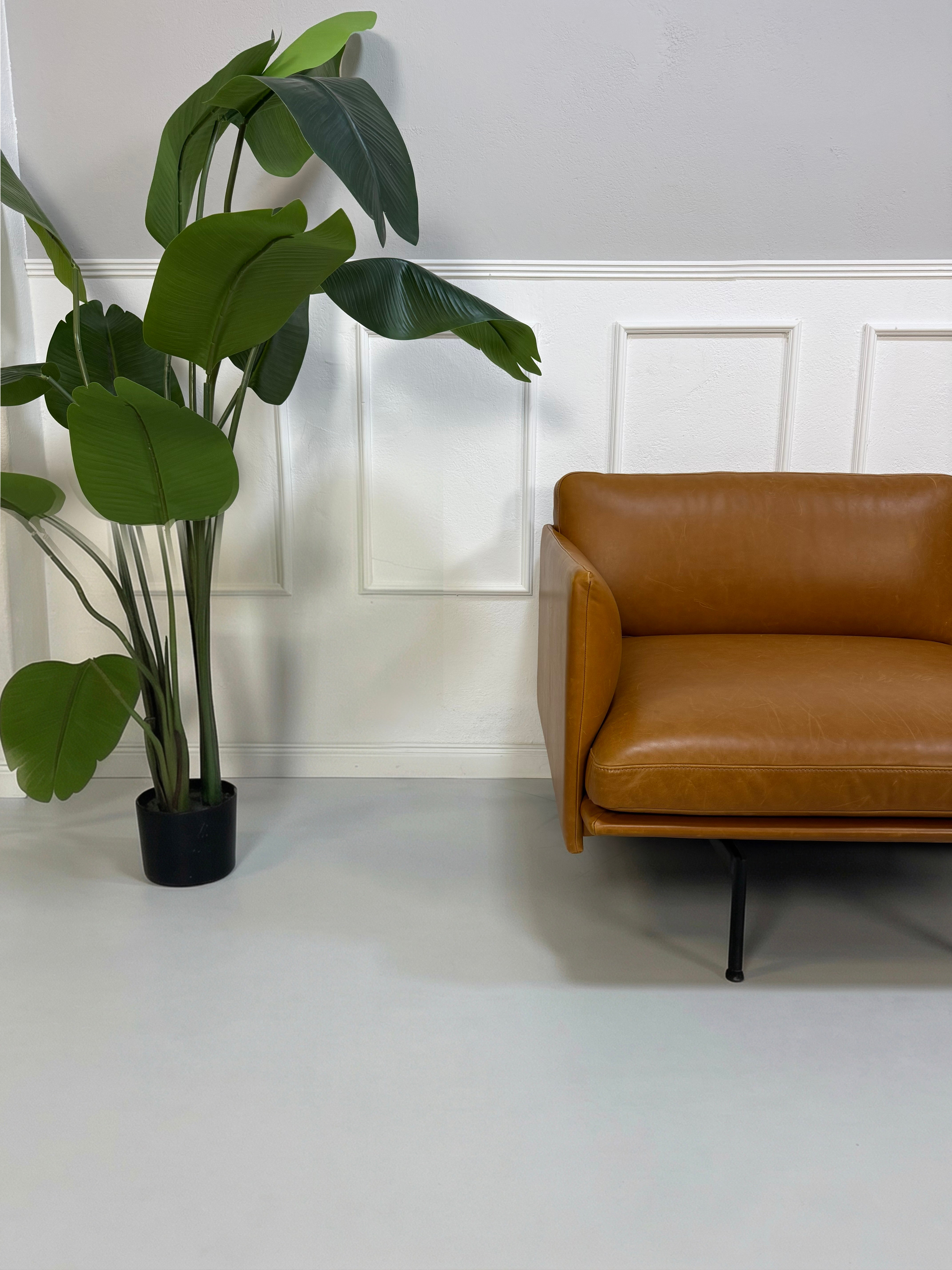 Gebrauchtes braunes cognac Muuto Outline Designer Leder Sofa vor einer Wand, stilvoll und modern eingerichtet.