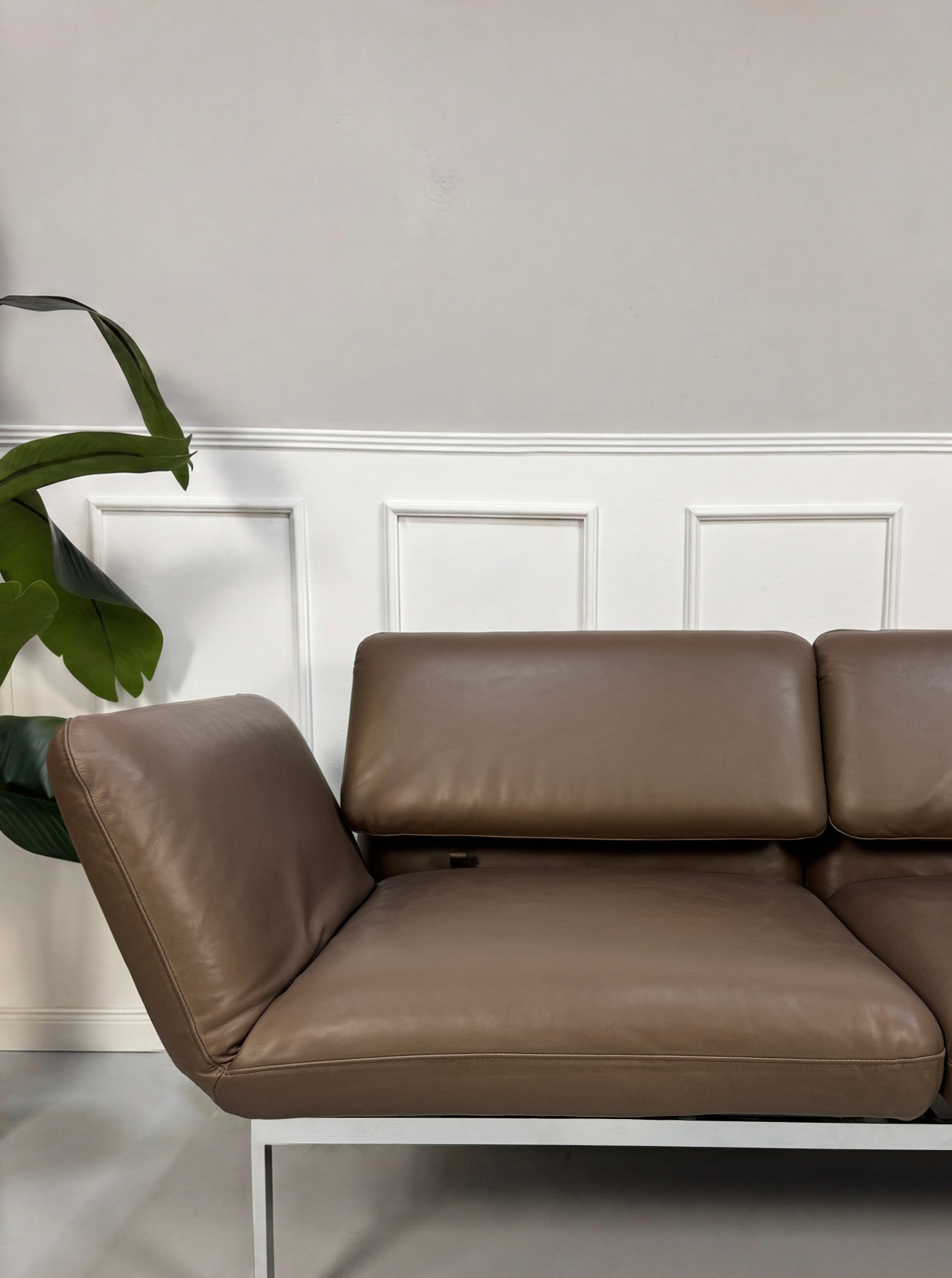 Gebrauchtes braunes Brühl Roro Designer Leder Sofa vor einer Wand, stilvoll und modern eingerichtet.