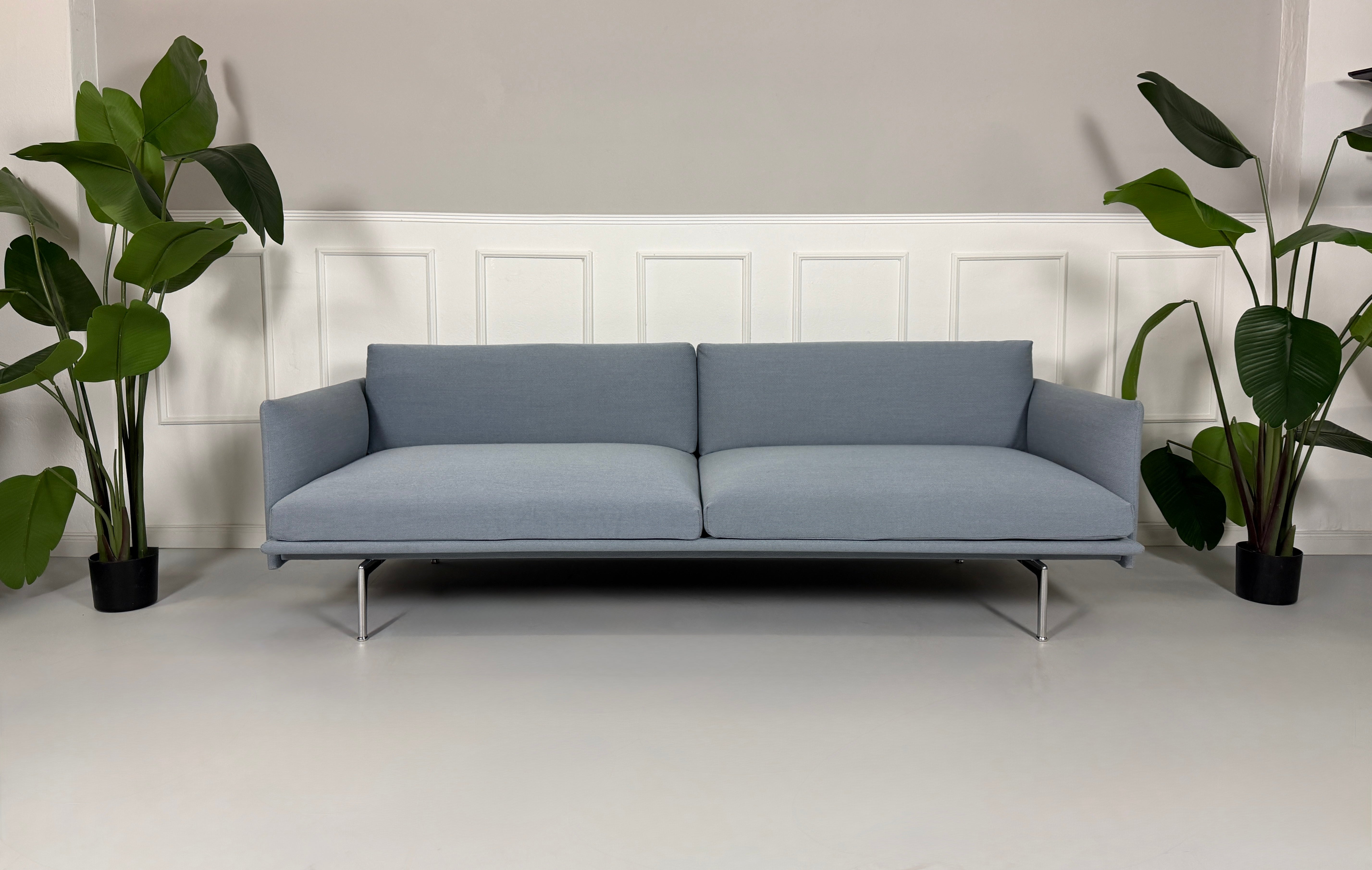 Gebrauchtes blaues Muuto Outline Designer Stoff Sofa vor einer Wand, stilvoll und modern eingerichtet.