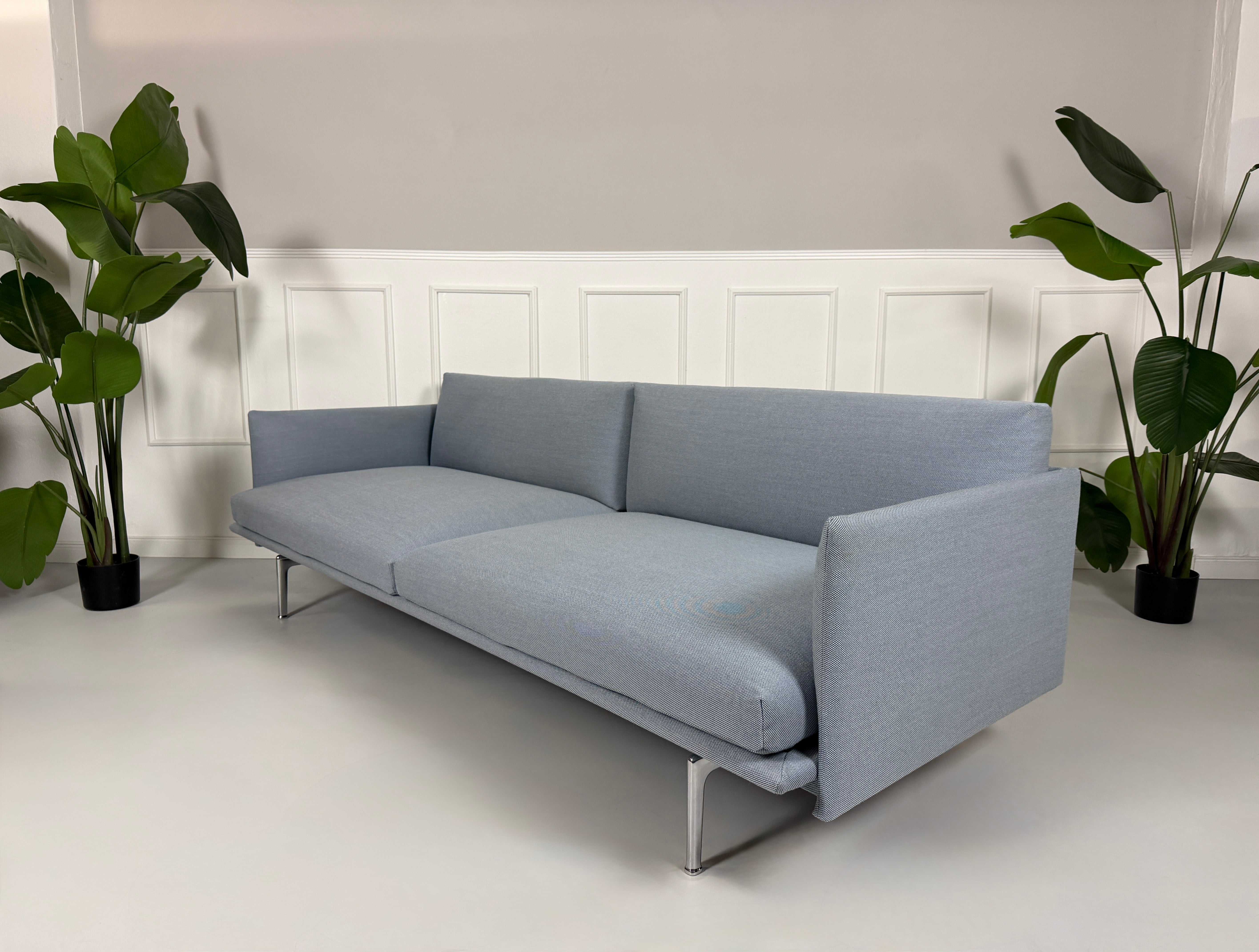 Gebrauchtes blaues Muuto Outline Designer Stoff Sofa vor einer Wand, stilvoll und modern eingerichtet.
