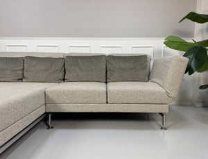 Gebrauchtes graues Brühl Moule Designer Stoff Sofa vor einer Wand, stilvoll und modern eingerichtet.