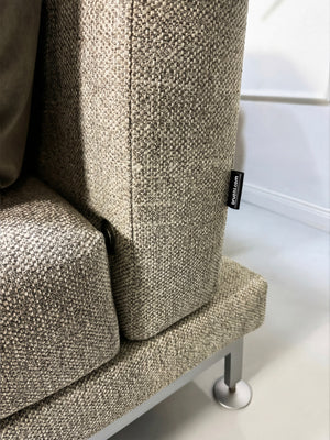 Gebrauchtes graues Brühl Moule Designer Stoff Sofa vor einer Wand, stilvoll und modern eingerichtet.