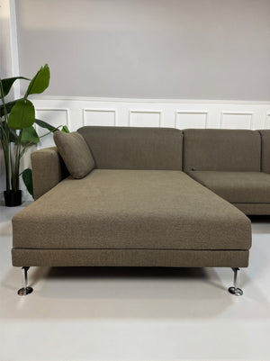Gebrauchtes braunes Brühl Moule Designer Stoff Sofa vor einer Wand, stilvoll und modern eingerichtet.