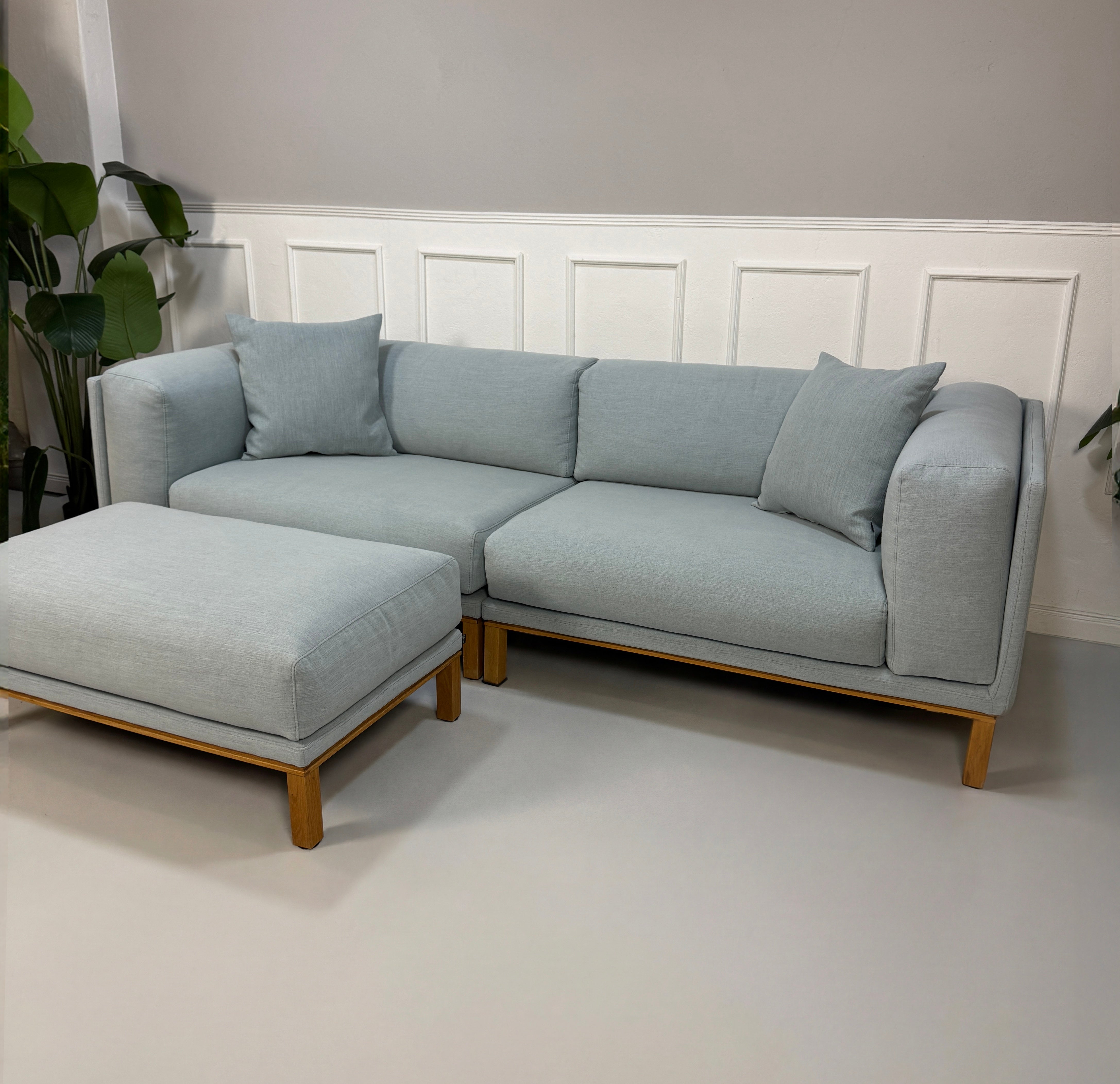 Gebrauchtes blaues Bolia Cosy Designer Stoff Sofa mit Hocker vor einer Wand, stilvoll und modern eingerichtet.