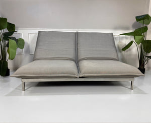 Gebrauchtes graues Rolf Benz Nova Designer Stoff Sofa vor einer Wand, stilvoll und modern eingerichtet.