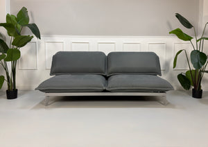 Gebrauchtes graues Rolf Benz Nova Designer Stoff Sofa vor einer Wand, stilvoll und modern eingerichtet.