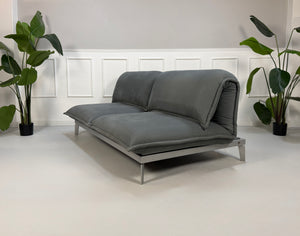 Gebrauchtes graues Rolf Benz Nova Designer Stoff Sofa vor einer Wand, stilvoll und modern eingerichtet.