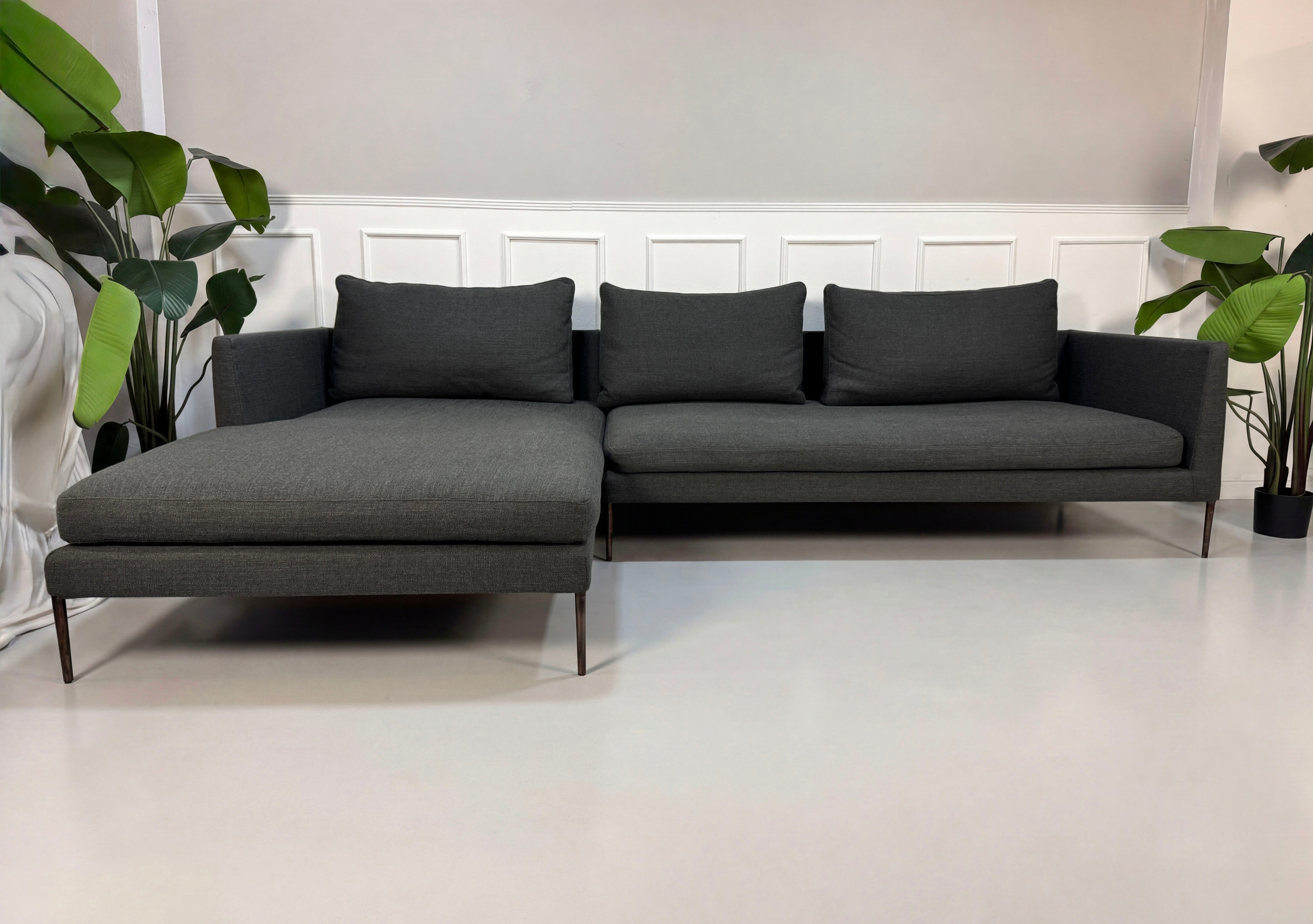 Gebrauchtes graues COR Pilotis Designer Stoff Sofa vor einer Wand, stilvoll und modern eingerichtet.
