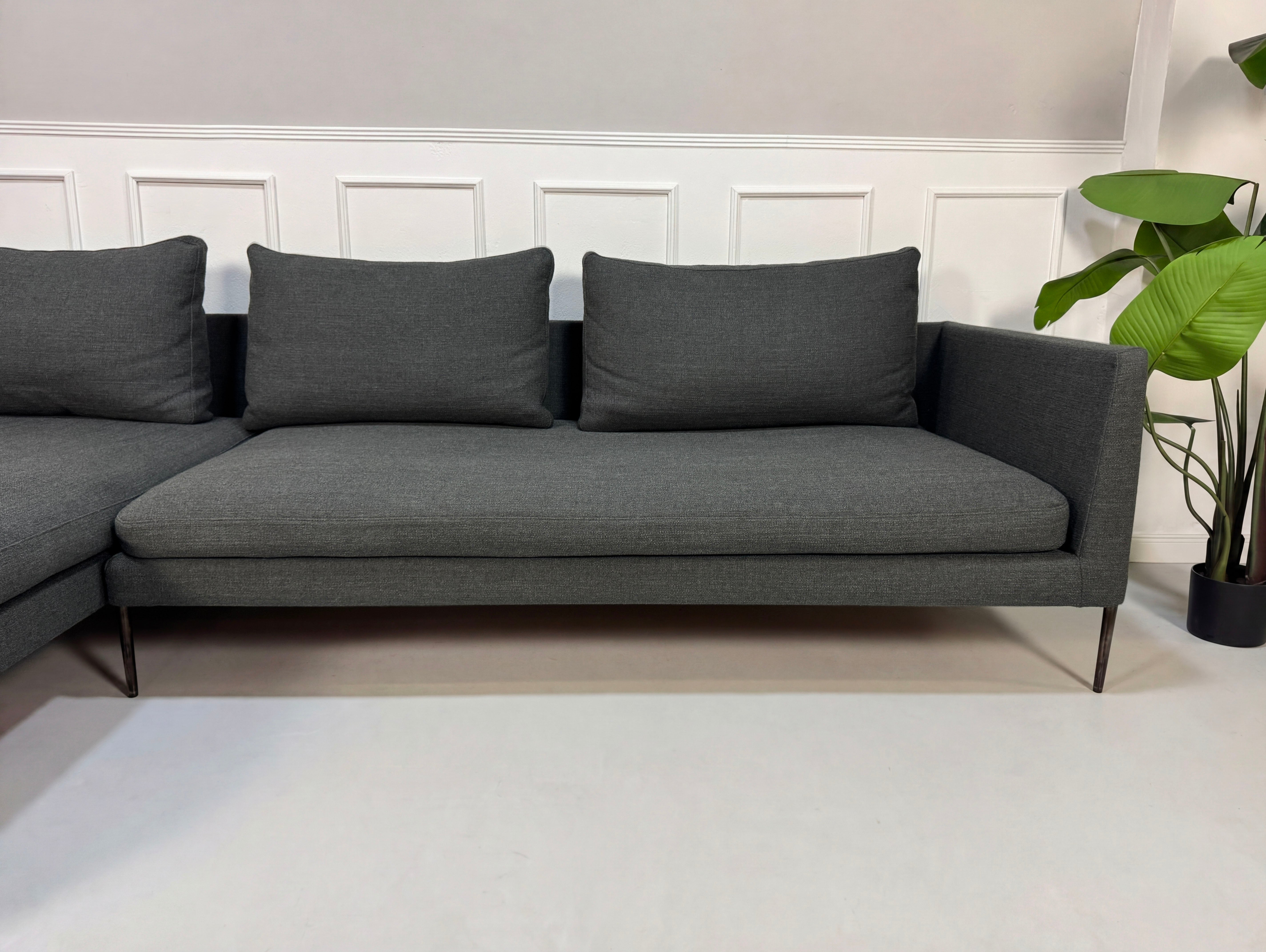 Gebrauchtes graues COR Pilotis Designer Stoff Sofa vor einer Wand, stilvoll und modern eingerichtet.