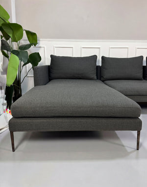 Gebrauchtes graues COR Pilotis Designer Stoff Sofa vor einer Wand, stilvoll und modern eingerichtet.
