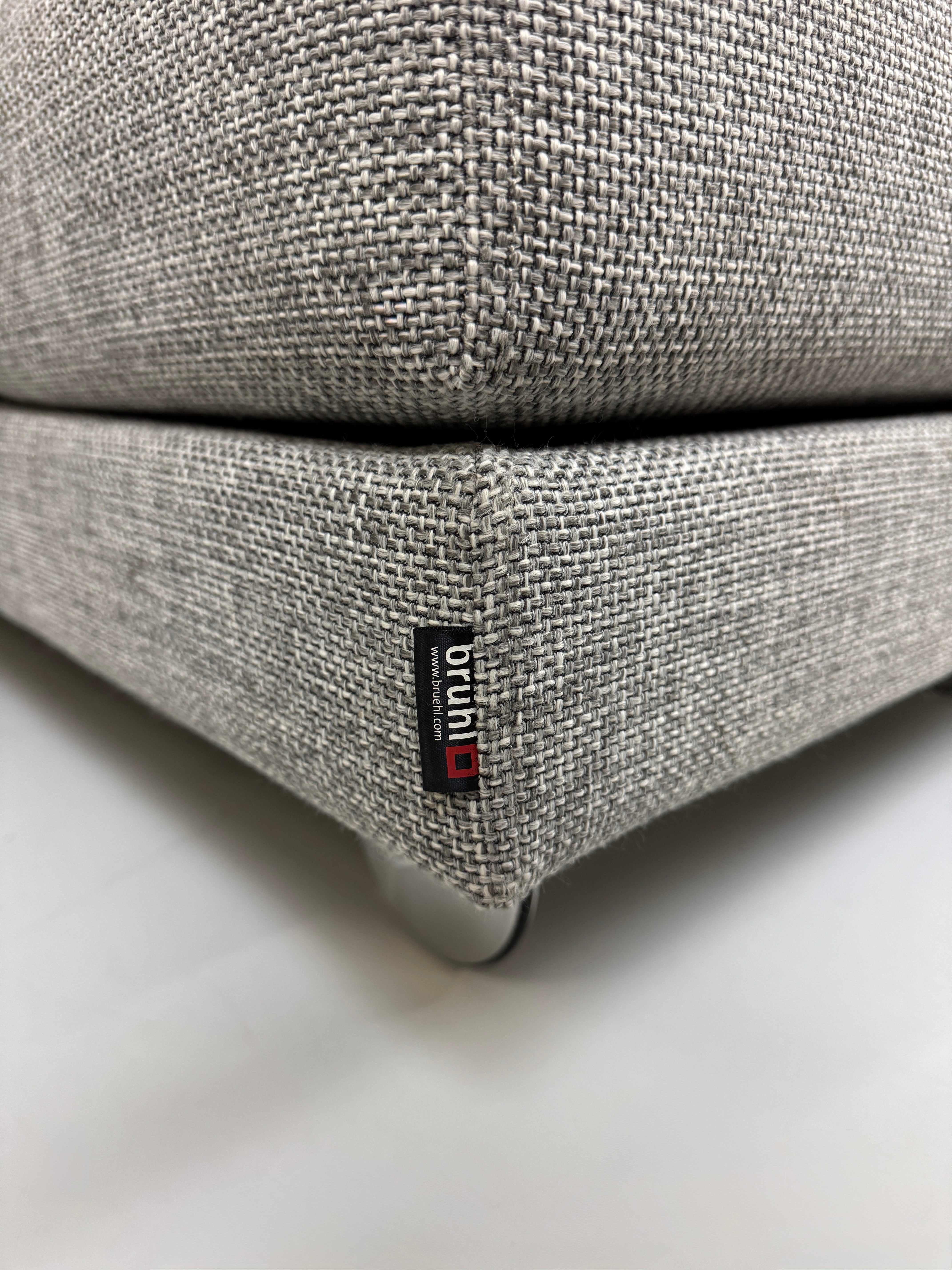 Gebrauchtes graues Brühl Four Two Designer Stoff Sofa vor einer Wand, stilvoll und modern eingerichtet.