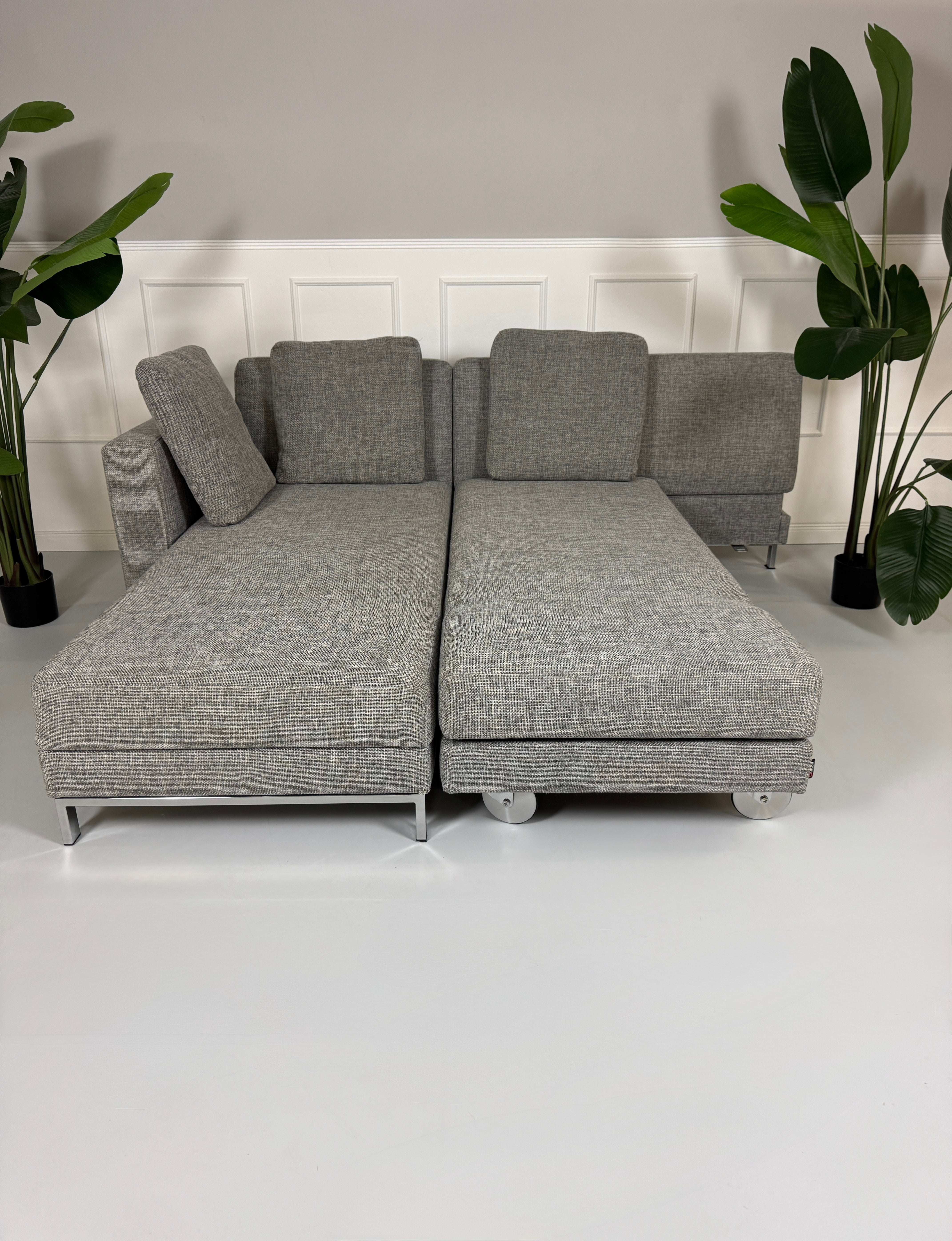 Gebrauchtes graues Brühl Four Two Designer Stoff Sofa vor einer Wand, stilvoll und modern eingerichtet.