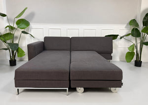 Gebrauchtes grau blaues Brühl Four Two Designer Stoff Sofa vor einer Wand, stilvoll und modern eingerichtet.