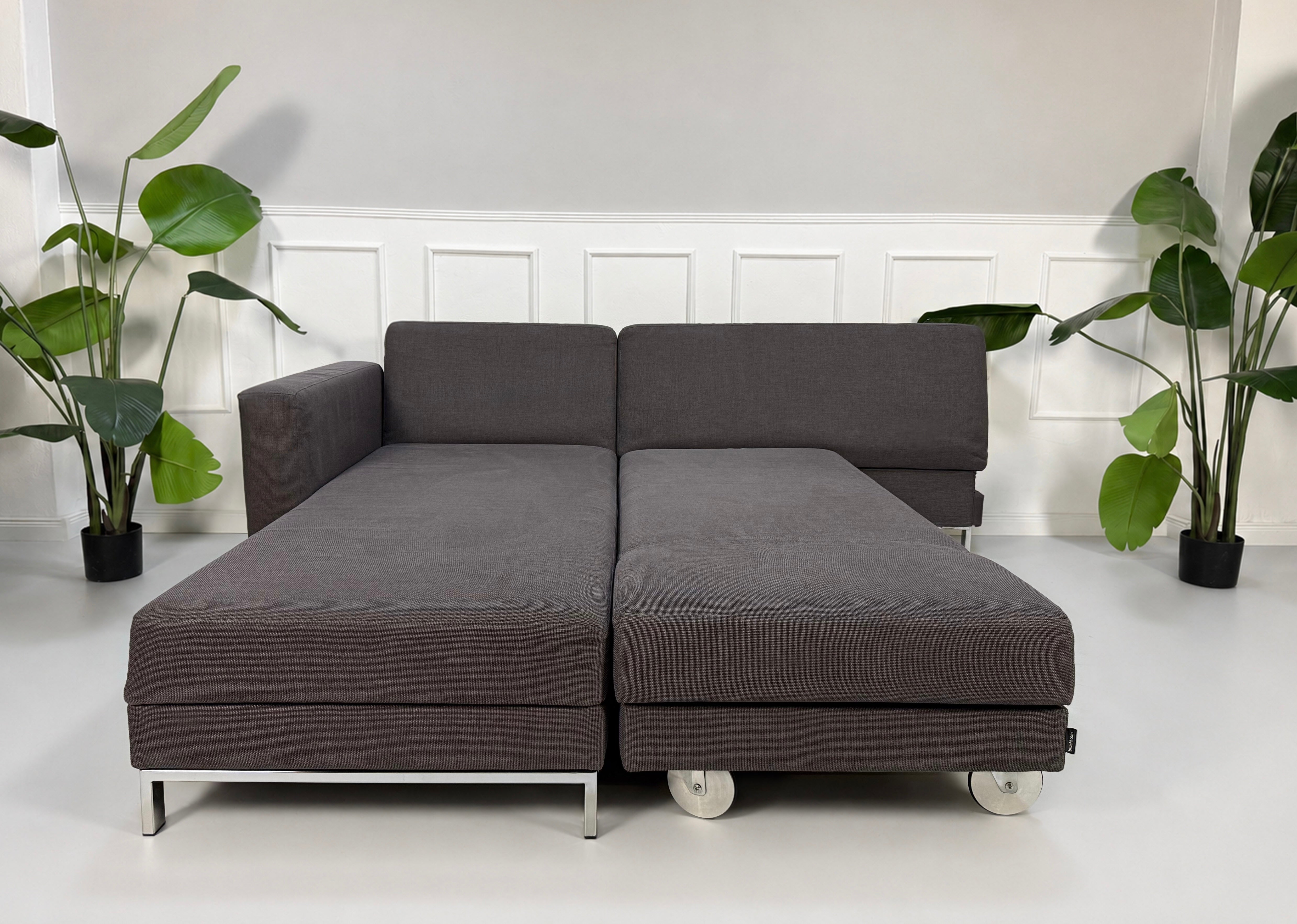 Gebrauchtes grau blaues Brühl Four Two Designer Stoff Sofa vor einer Wand, stilvoll und modern eingerichtet.