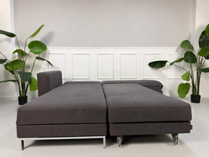 Gebrauchtes grau blaues Brühl Four Two Designer Stoff Sofa vor einer Wand, stilvoll und modern eingerichtet.