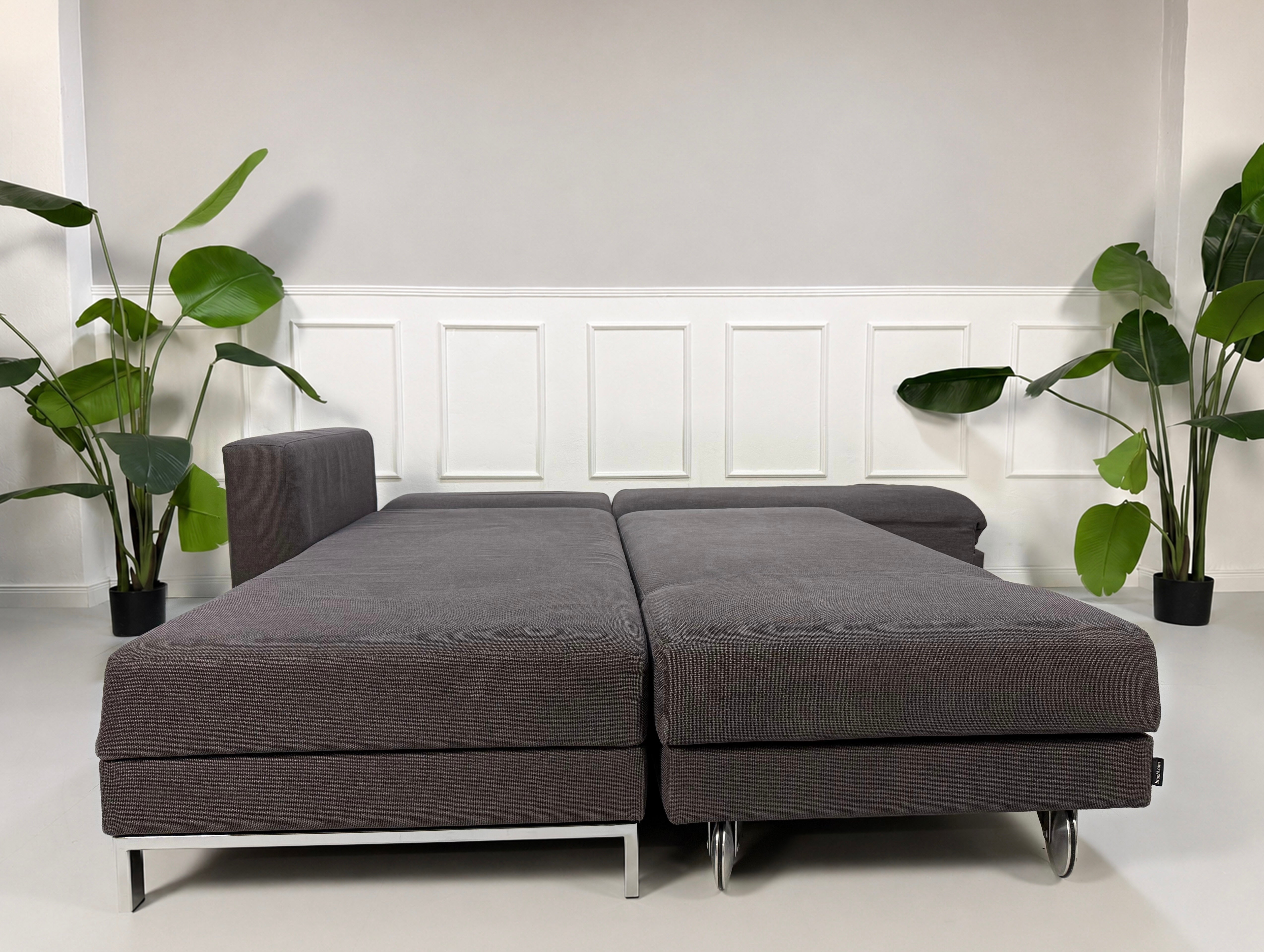 Gebrauchtes grau blaues Brühl Four Two Designer Stoff Sofa vor einer Wand, stilvoll und modern eingerichtet.