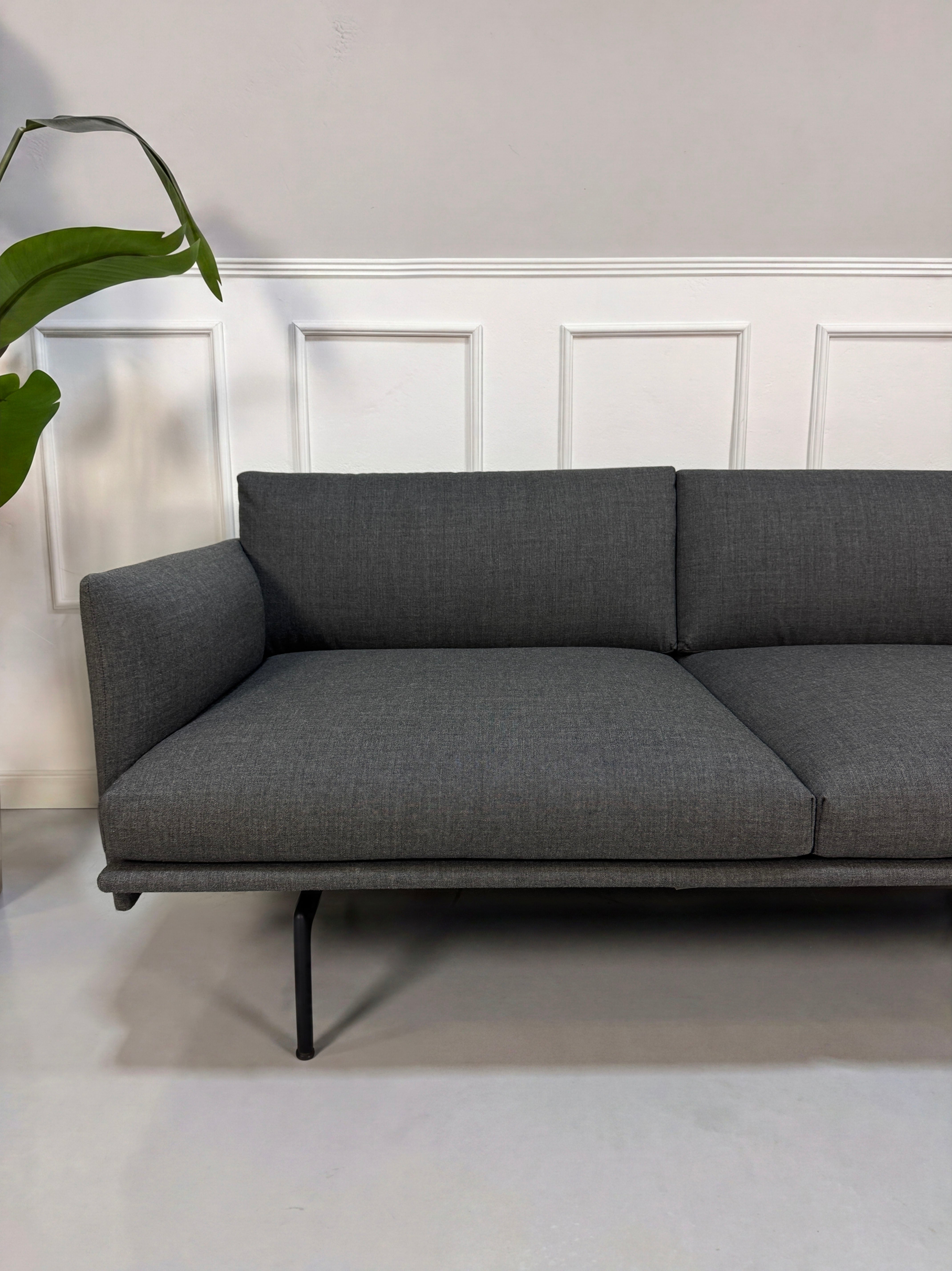 Gebrauchtes graues Muuto Outline Designer Stoff Sofa vor einer Wand, stilvoll und modern eingerichtet.