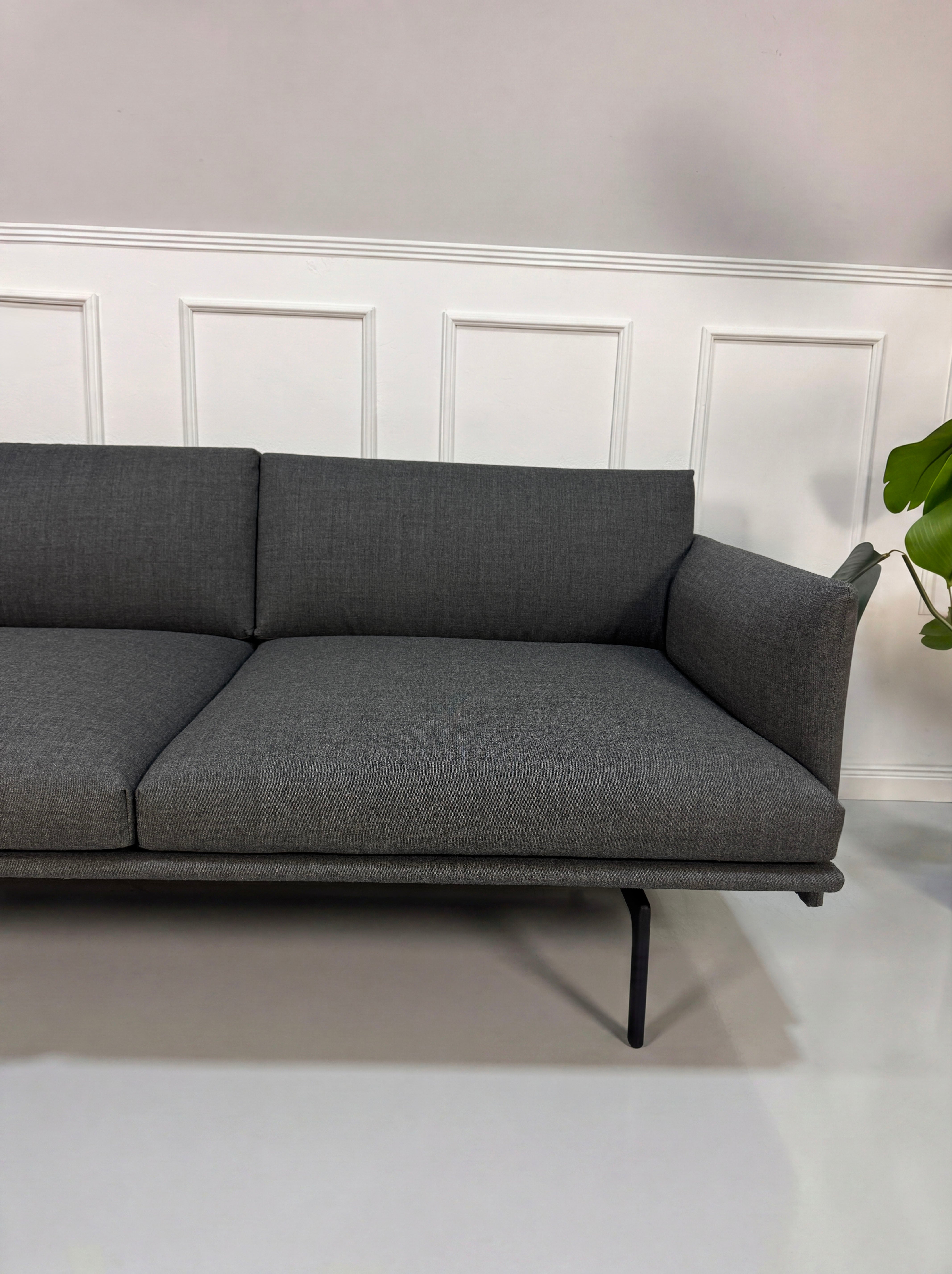 Gebrauchtes graues Muuto Outline Designer Stoff Sofa vor einer Wand, stilvoll und modern eingerichtet.