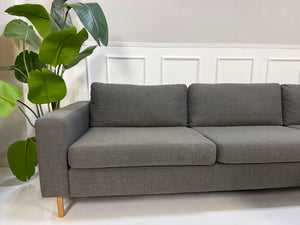 Gebrauchtes graues Bolia Scandinavia Designer Stoff Sofa vor einer Wand, stilvoll und modern eingerichtet.