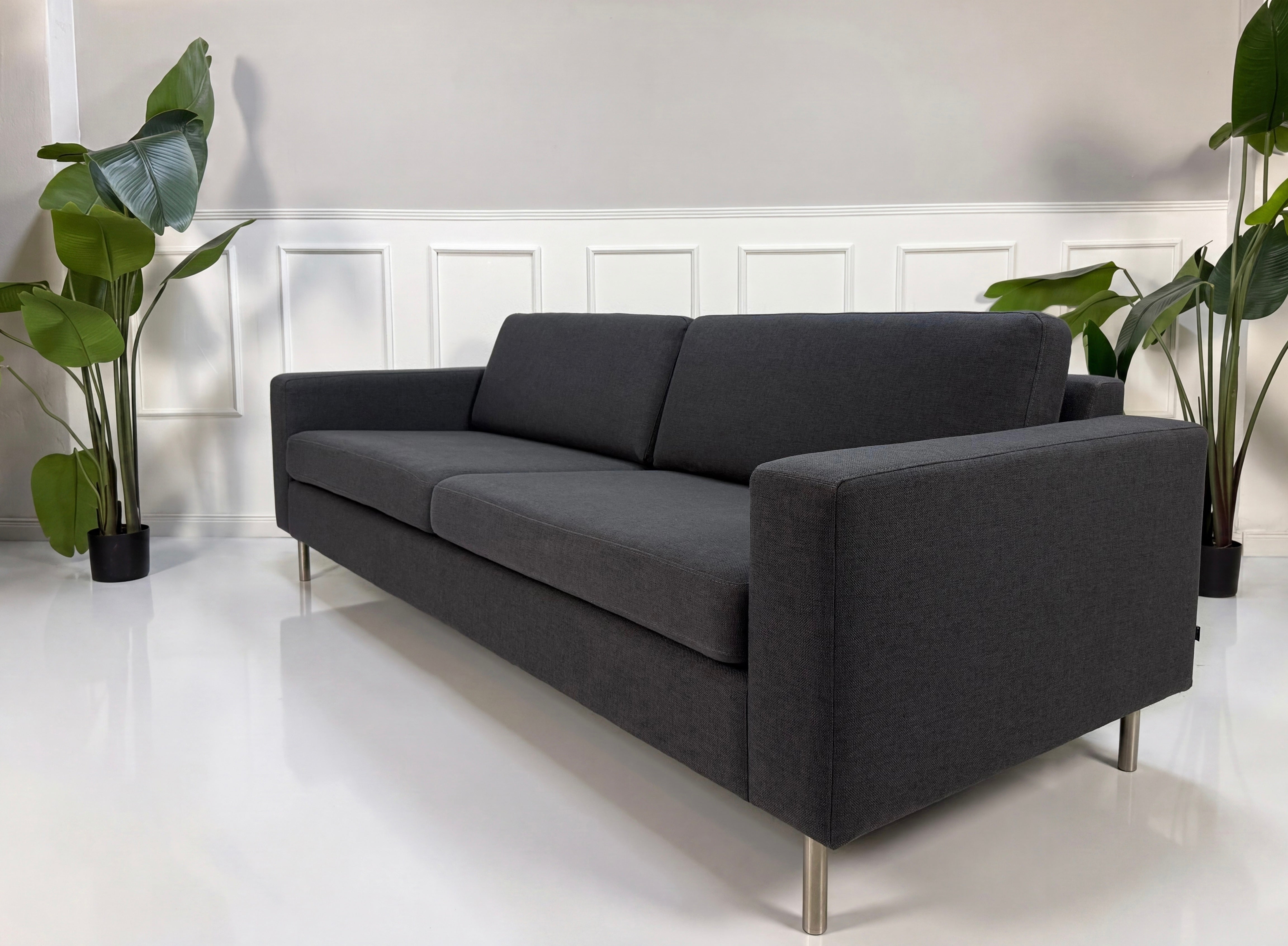 Gebrauchtes graues Bolia Scandinavia Designer Stoff Sofa vor einer Wand, stilvoll und modern eingerichtet.