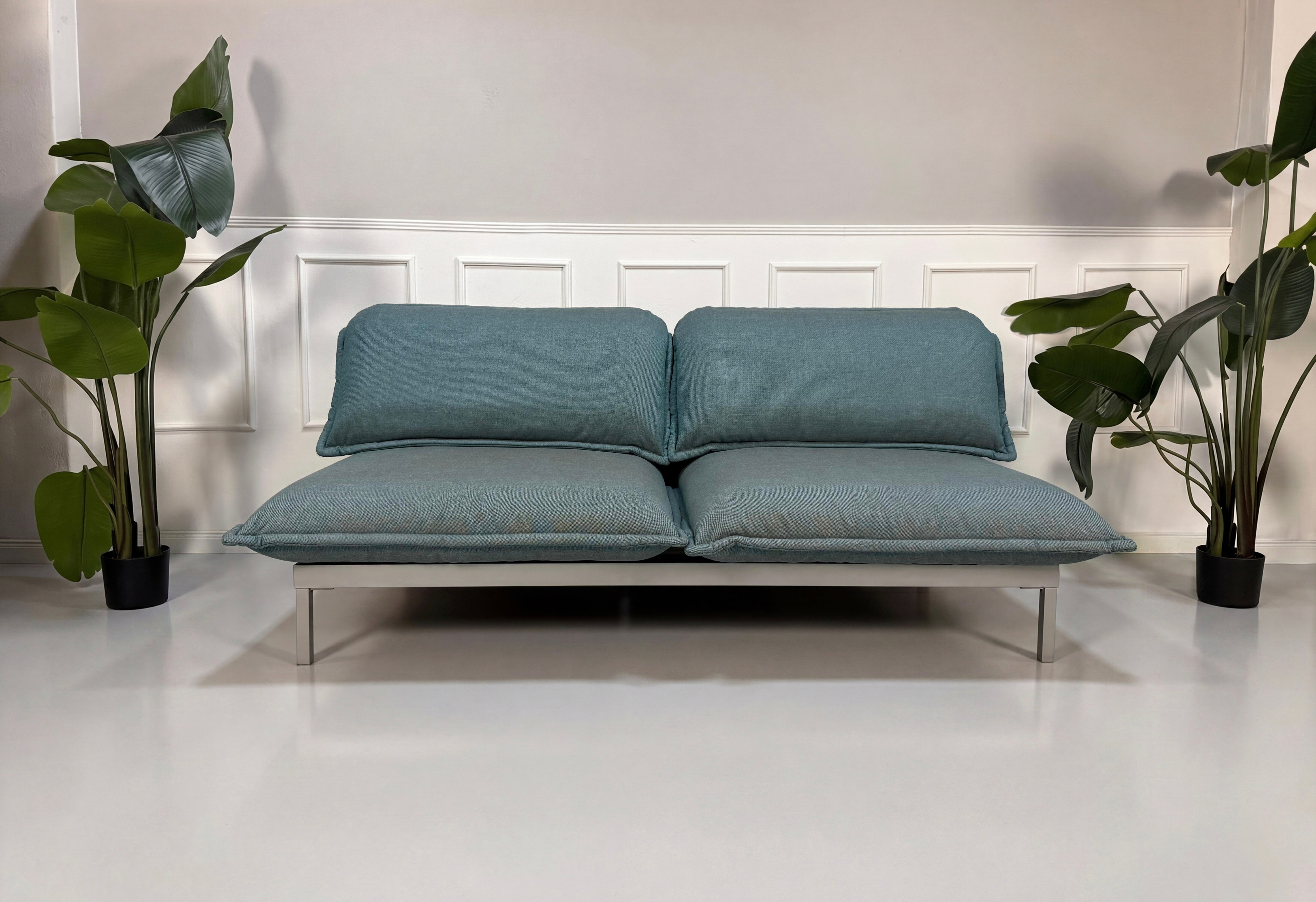 Gebrauchtes blaues Rolf Benz Nova Designer Stoff Sofa vor einer Wand, stilvoll und modern eingerichtet.