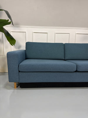 Gebrauchtes blaues Bolia Scandinavia Designer Stoff Sofa vor einer Wand, stilvoll und modern eingerichtet.