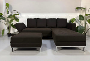 Gebrauchtes braunes Brühl Fourtwo Designer Stoff Sofa mit Hocker vor einer Wand, stilvoll und modern eingerichtet.
