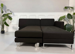 Gebrauchtes braunes Brühl Fourtwo Designer Stoff Sofa mit Hocker vor einer Wand, stilvoll und modern eingerichtet.
