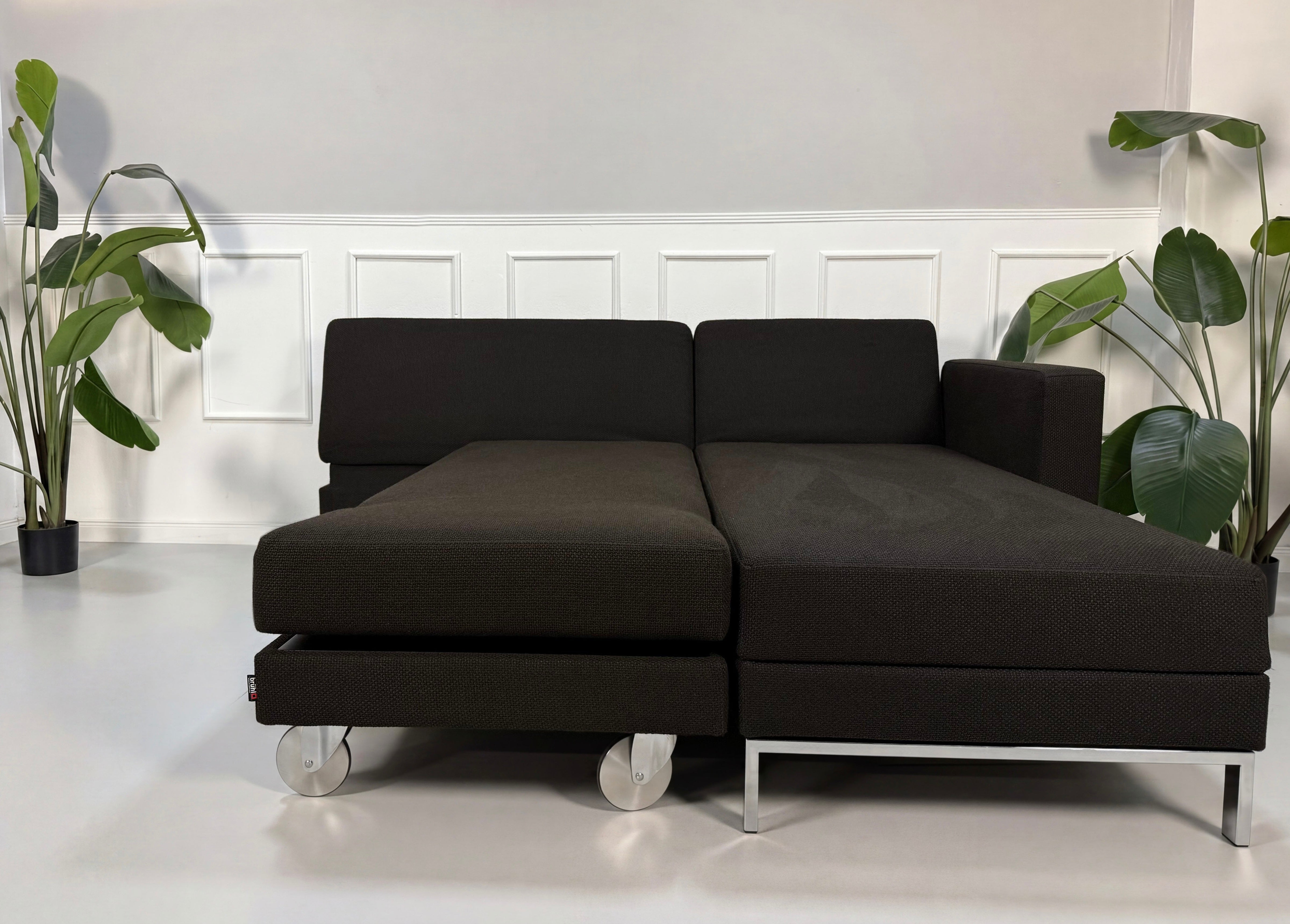 Gebrauchtes braunes Brühl Fourtwo Designer Stoff Sofa mit Hocker vor einer Wand, stilvoll und modern eingerichtet.