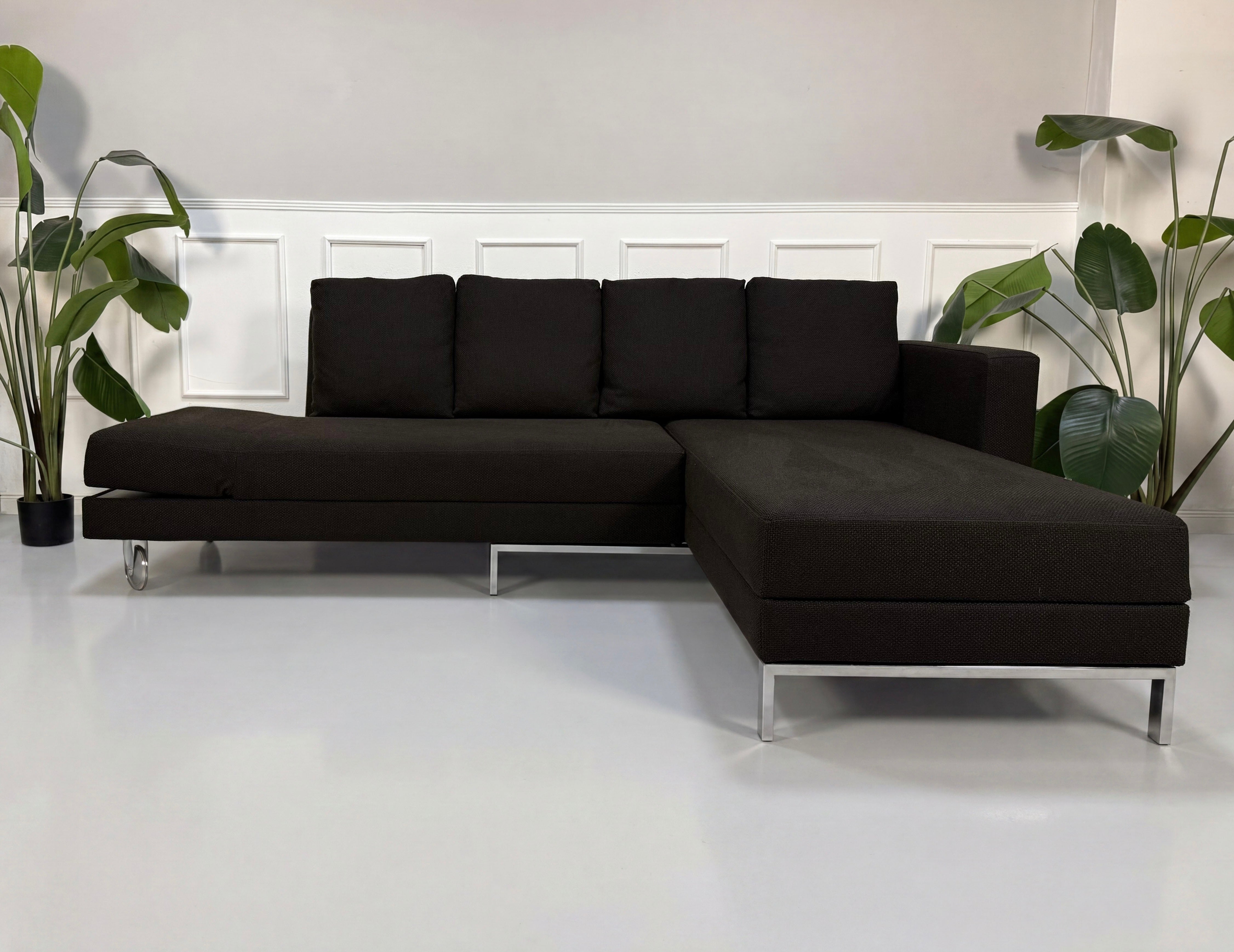 Gebrauchtes braunes Brühl Fourtwo Designer Stoff Sofa mit Hocker vor einer Wand, stilvoll und modern eingerichtet.