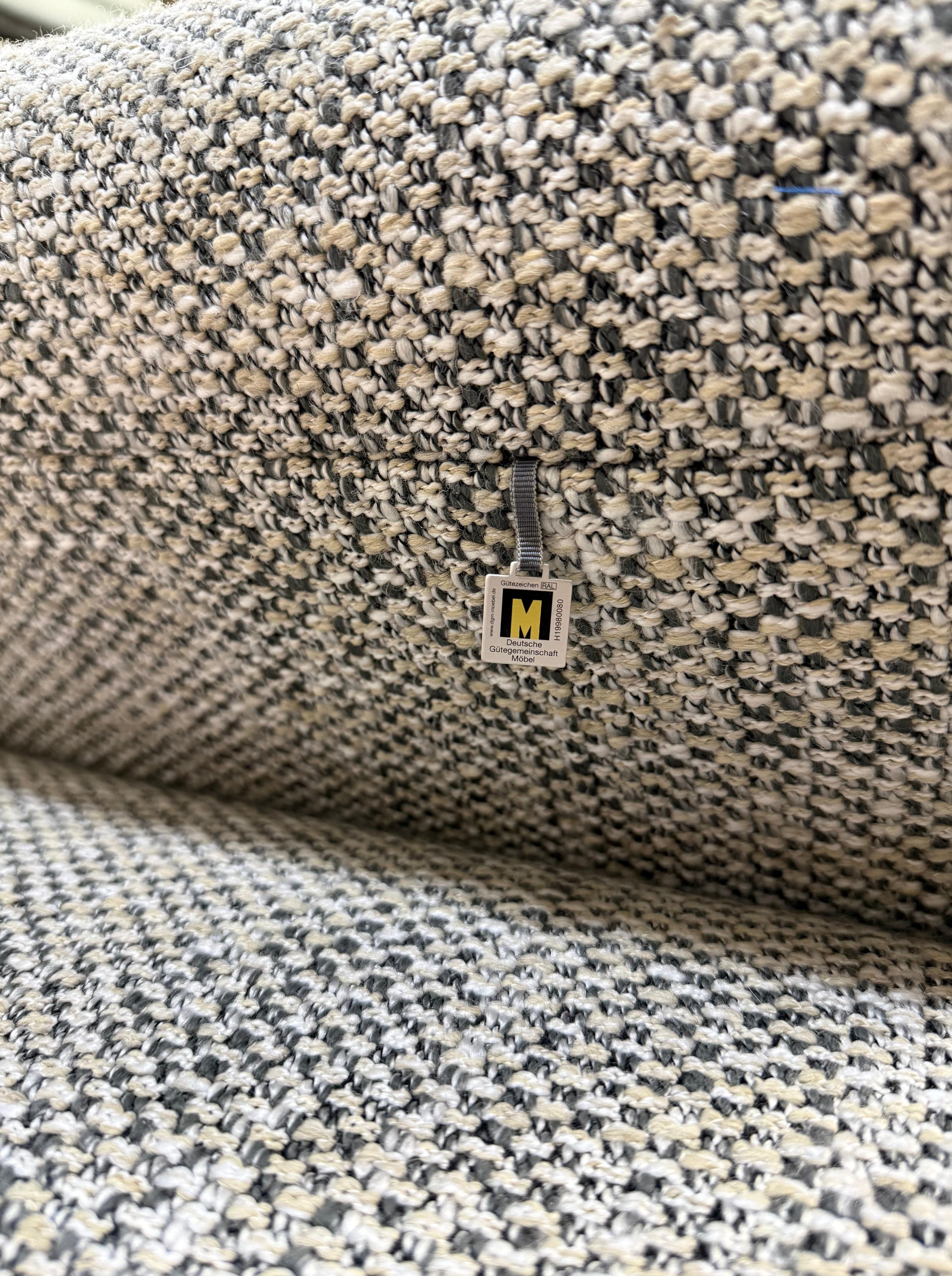 Gebrauchtes graues Koinor Hiero Designer Stoff Sofa vor einer Wand, stilvoll und modern eingerichtet.