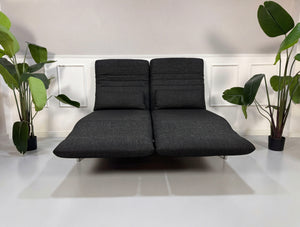 Gebrauchtes graues Rolf Benz Plura Designer Stoff Sofa mit Hocker vor einer Wand, stilvoll und modern eingerichtet.