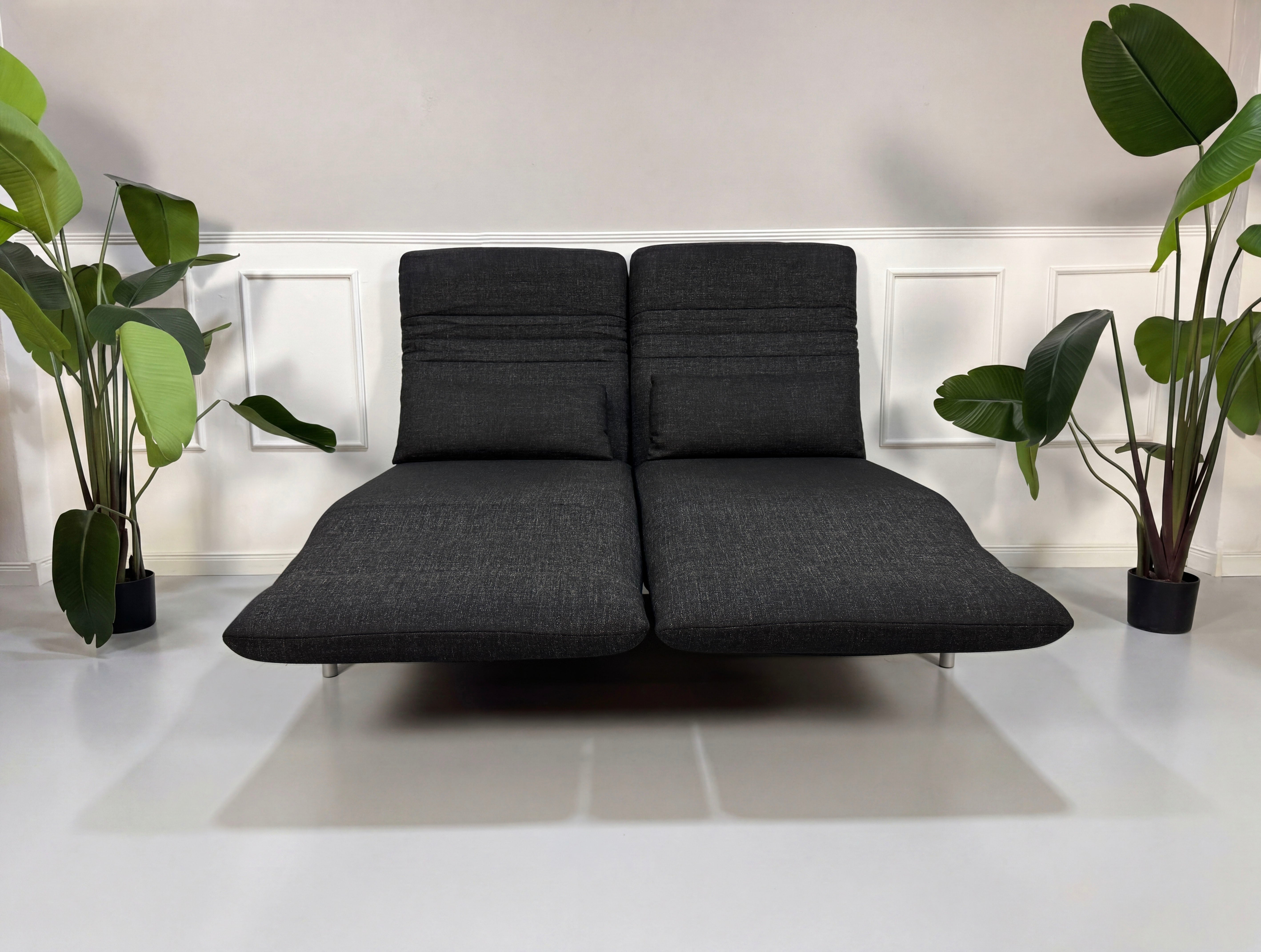 Gebrauchtes graues Rolf Benz Plura Designer Stoff Sofa mit Hocker vor einer Wand, stilvoll und modern eingerichtet.