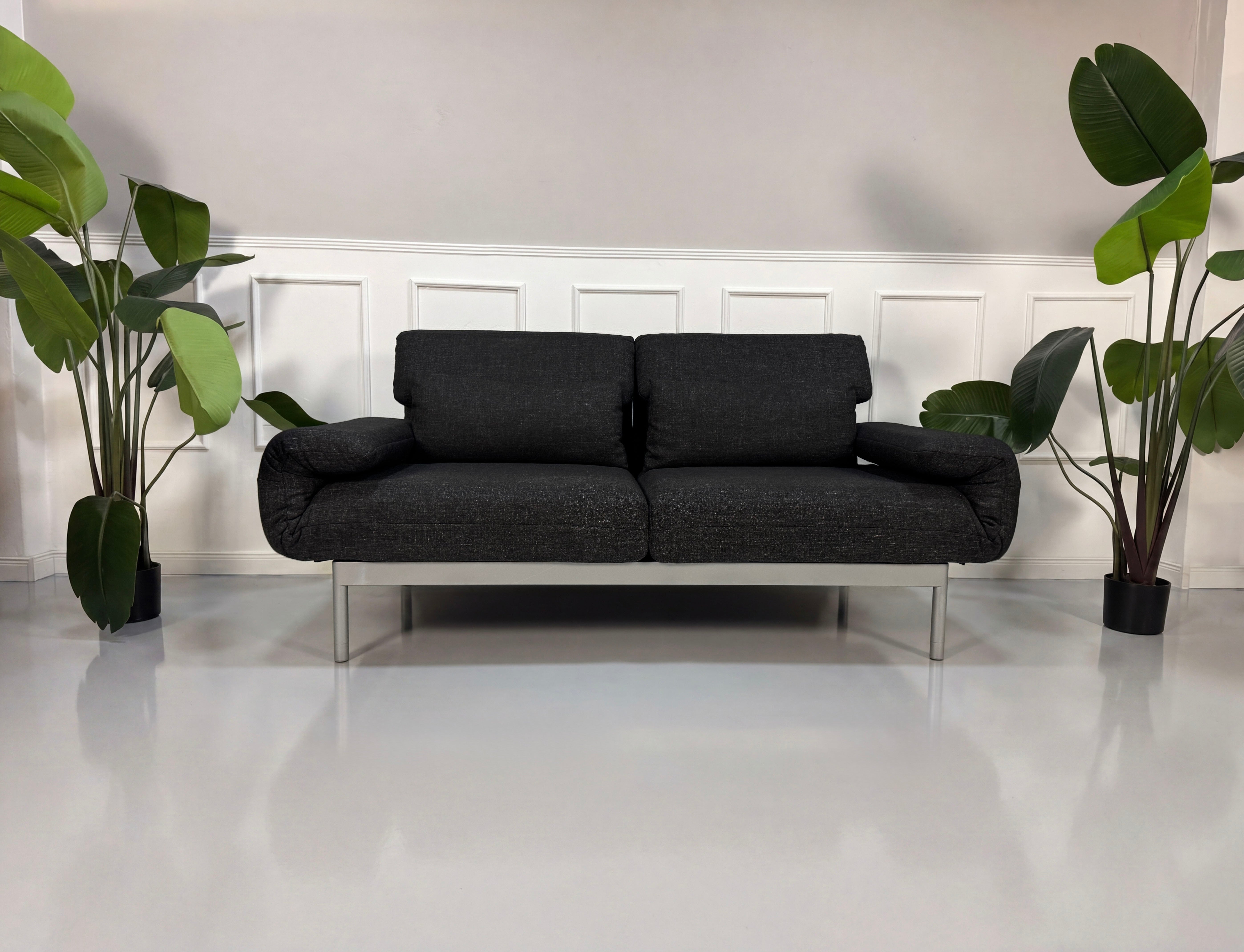 Gebrauchtes graues Rolf Benz Plura Designer Stoff Sofa mit Hocker vor einer Wand, stilvoll und modern eingerichtet.