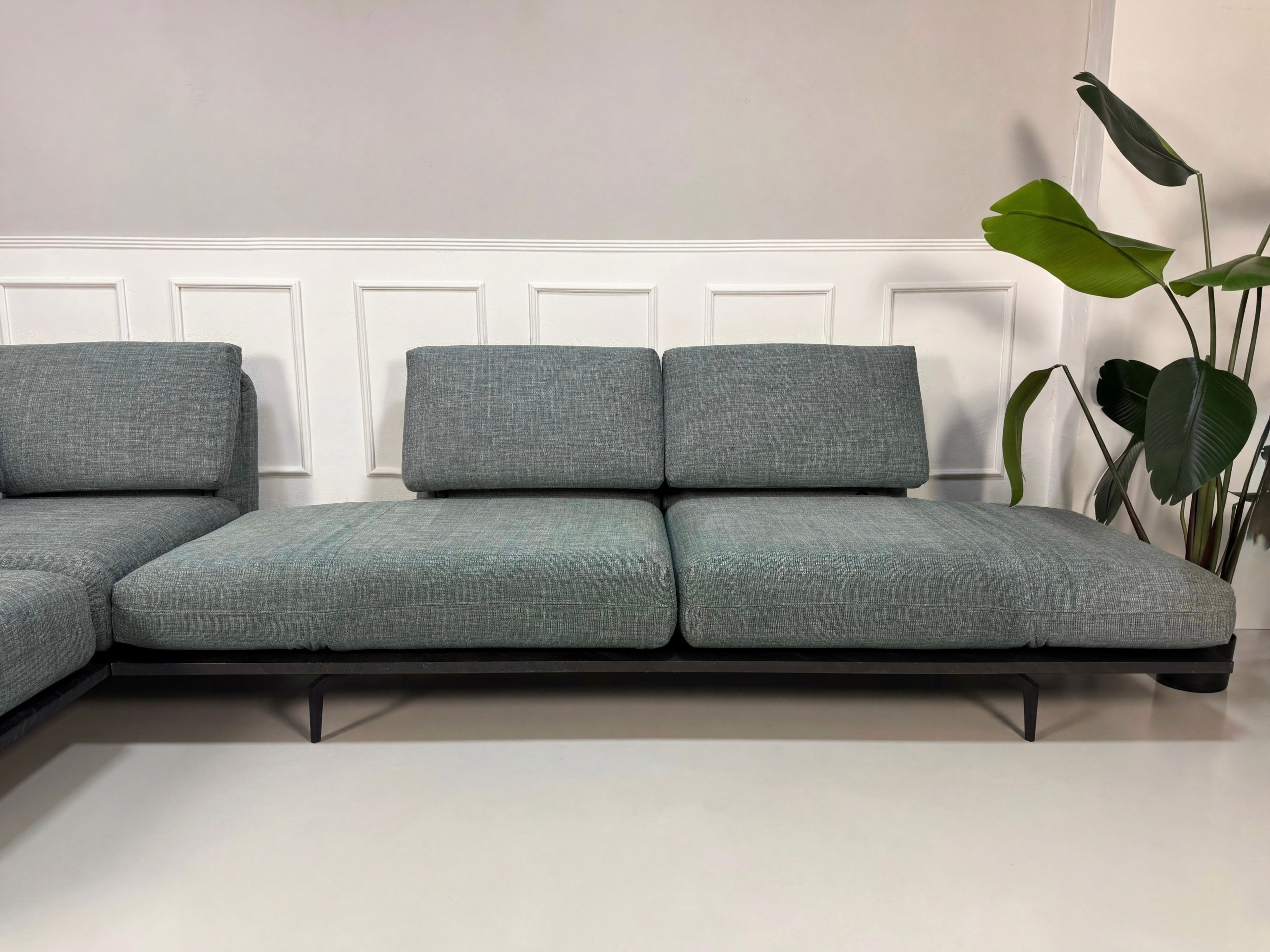 Gebrauchtes blau graues Rolf Benz Aura Designer Stoff Sofa vor einer Wand, stilvoll und modern eingerichtet.