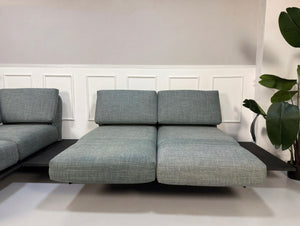 Gebrauchtes blau graues Rolf Benz Aura Designer Stoff Sofa vor einer Wand, stilvoll und modern eingerichtet.