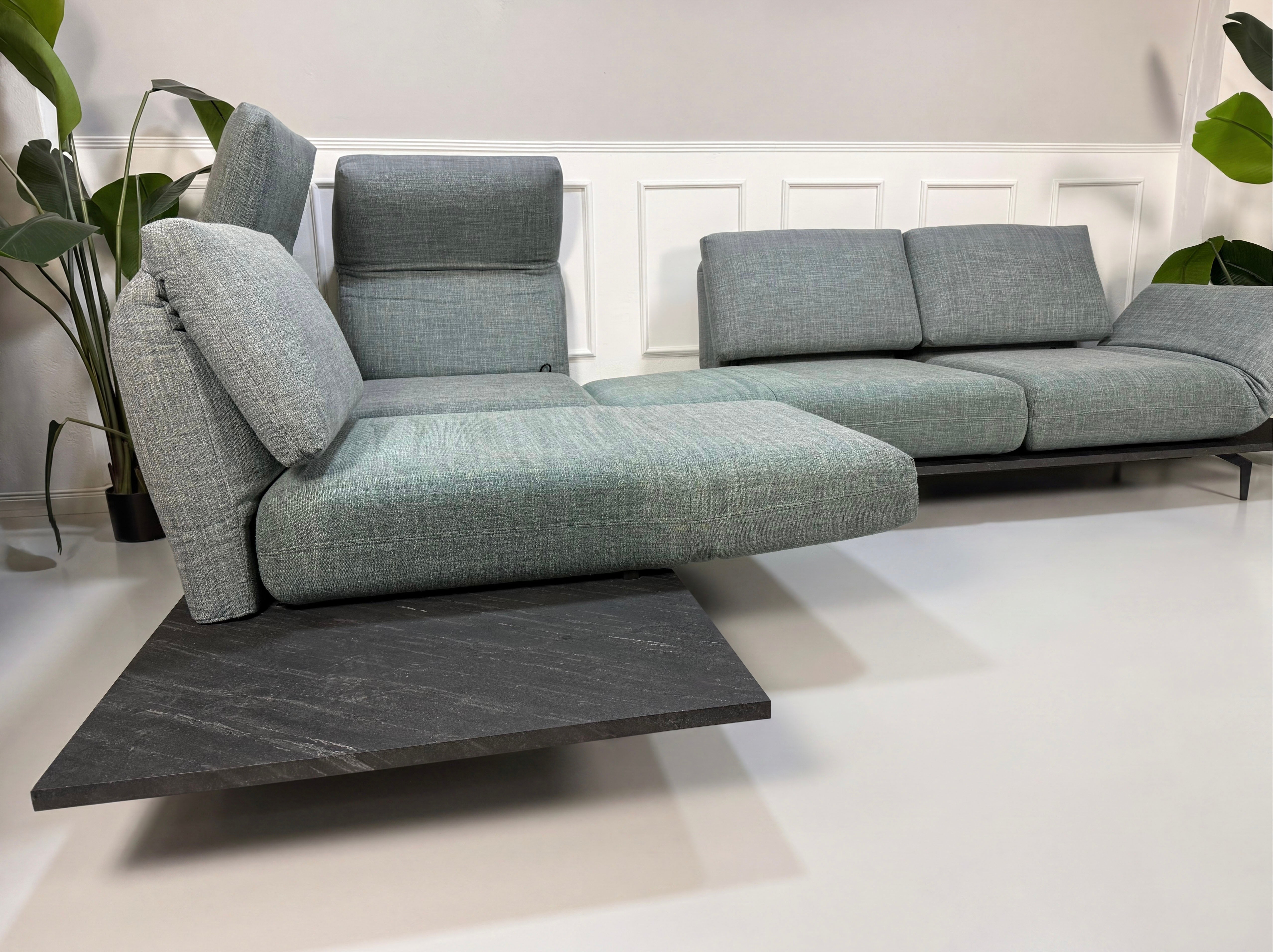 Gebrauchtes blau graues Rolf Benz Aura Designer Stoff Sofa vor einer Wand, stilvoll und modern eingerichtet.