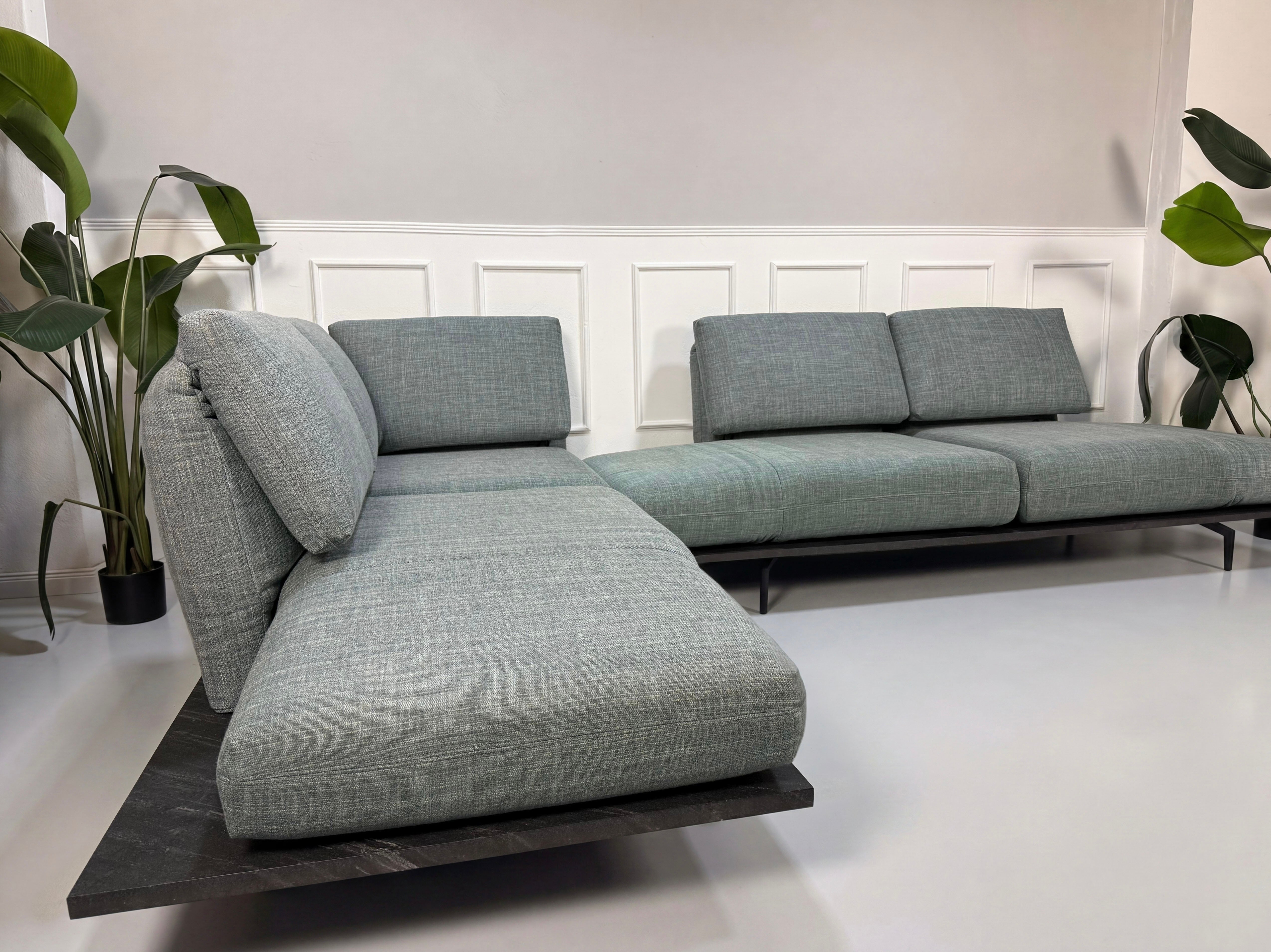 Gebrauchtes blau graues Rolf Benz Aura Designer Stoff Sofa vor einer Wand, stilvoll und modern eingerichtet.