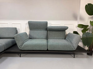 Gebrauchtes blau graues Rolf Benz Aura Designer Stoff Sofa vor einer Wand, stilvoll und modern eingerichtet.