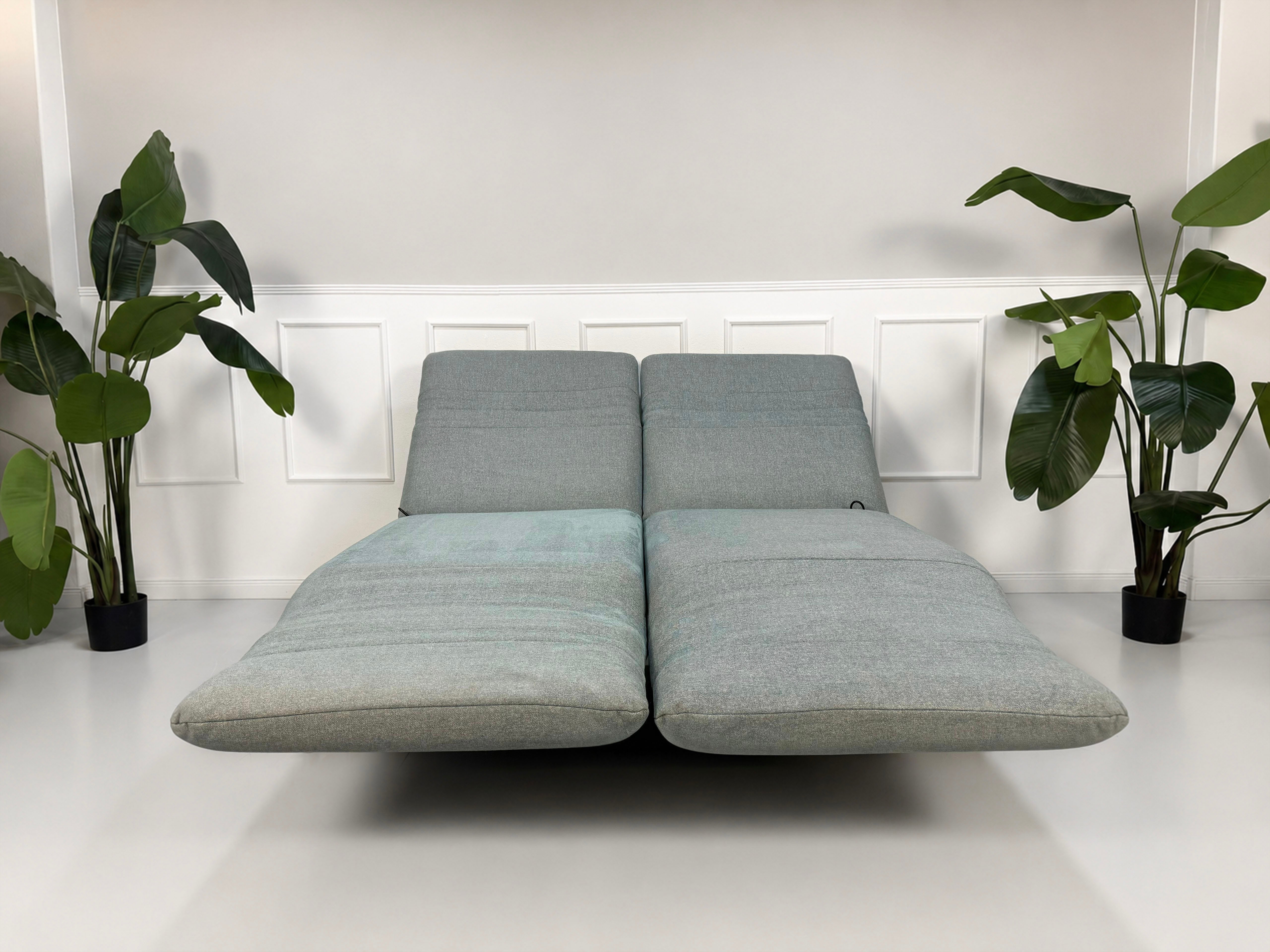 Gebrauchtes graues mint Rolf Benz Plura Designer Stoff Sofa vor einer Wand, stilvoll und modern eingerichtet.