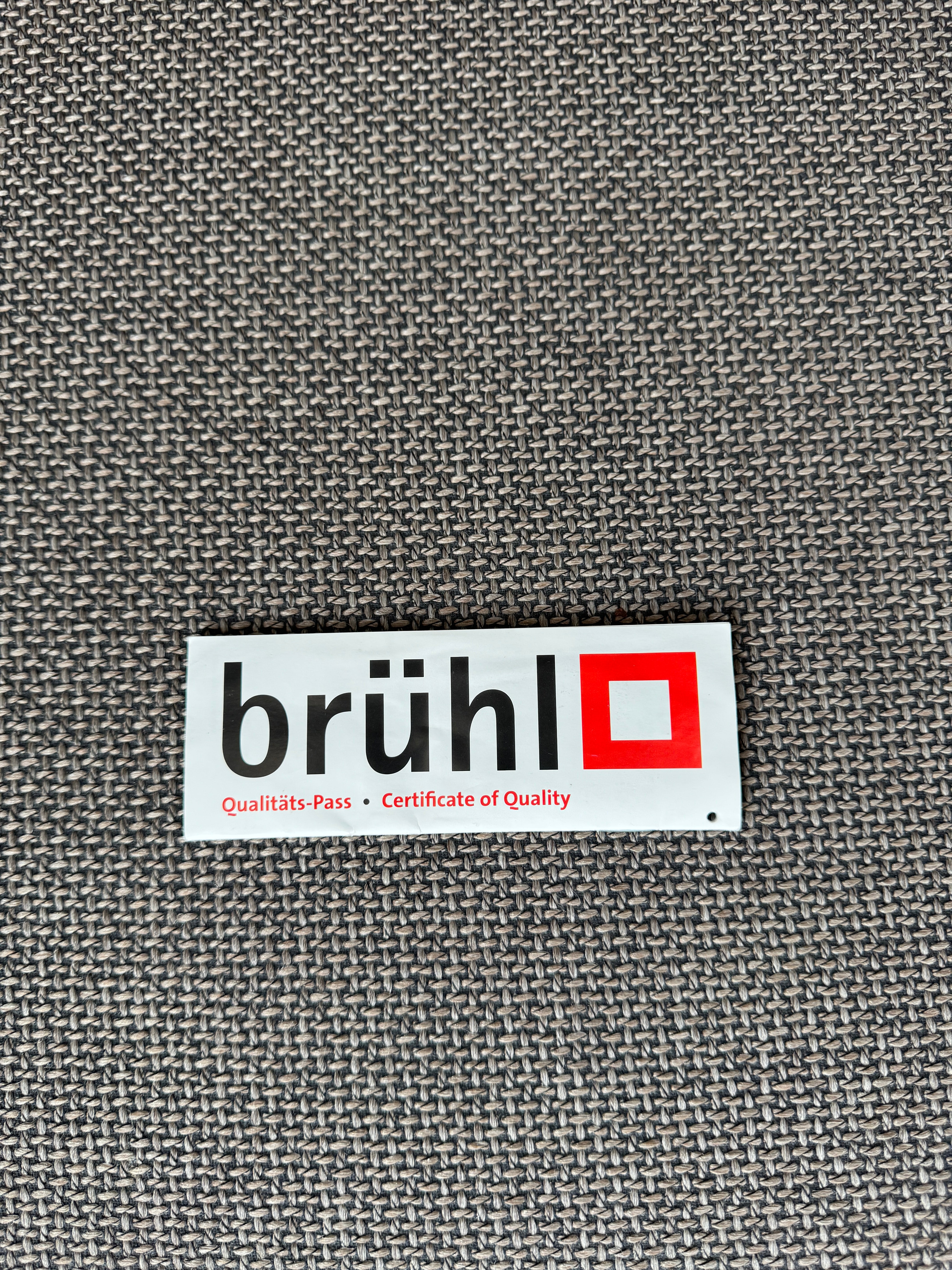 Gebrauchtes braun graues Brühl Moule Designer Stoff Sofa vor einer Wand, stilvoll und modern eingerichtet.