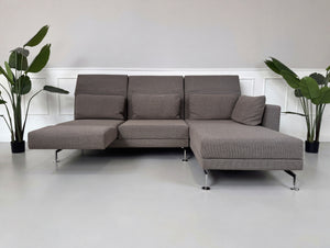 Gebrauchtes braun graues Brühl Moule Designer Stoff Sofa vor einer Wand, stilvoll und modern eingerichtet.