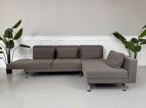 Gebrauchtes braun graues Brühl Moule Designer Stoff Sofa vor einer Wand, stilvoll und modern eingerichtet.