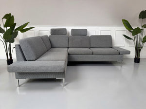 Gebrauchtes graues Brühl Alba Designer Stoff Sofa vor einer Wand, stilvoll und modern eingerichtet.