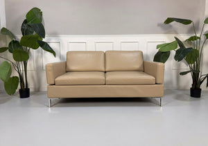 Gebrauchtes beiges Brühl Alba Designer Leder Sofa vor einer Wand, stilvoll und modern eingerichtet.

