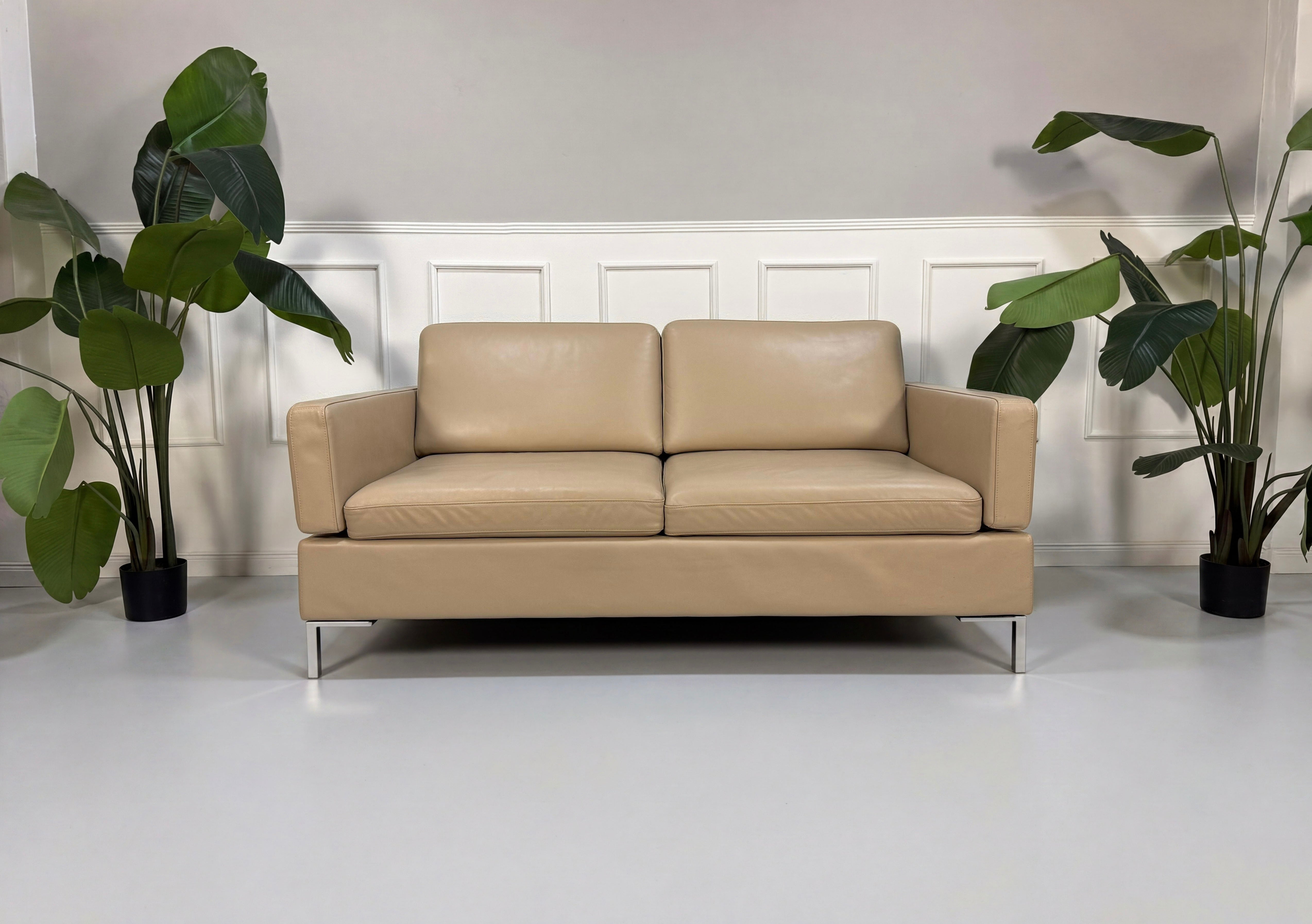 Gebrauchtes beiges Brühl Alba Designer Leder Sofa vor einer Wand, stilvoll und modern eingerichtet.

