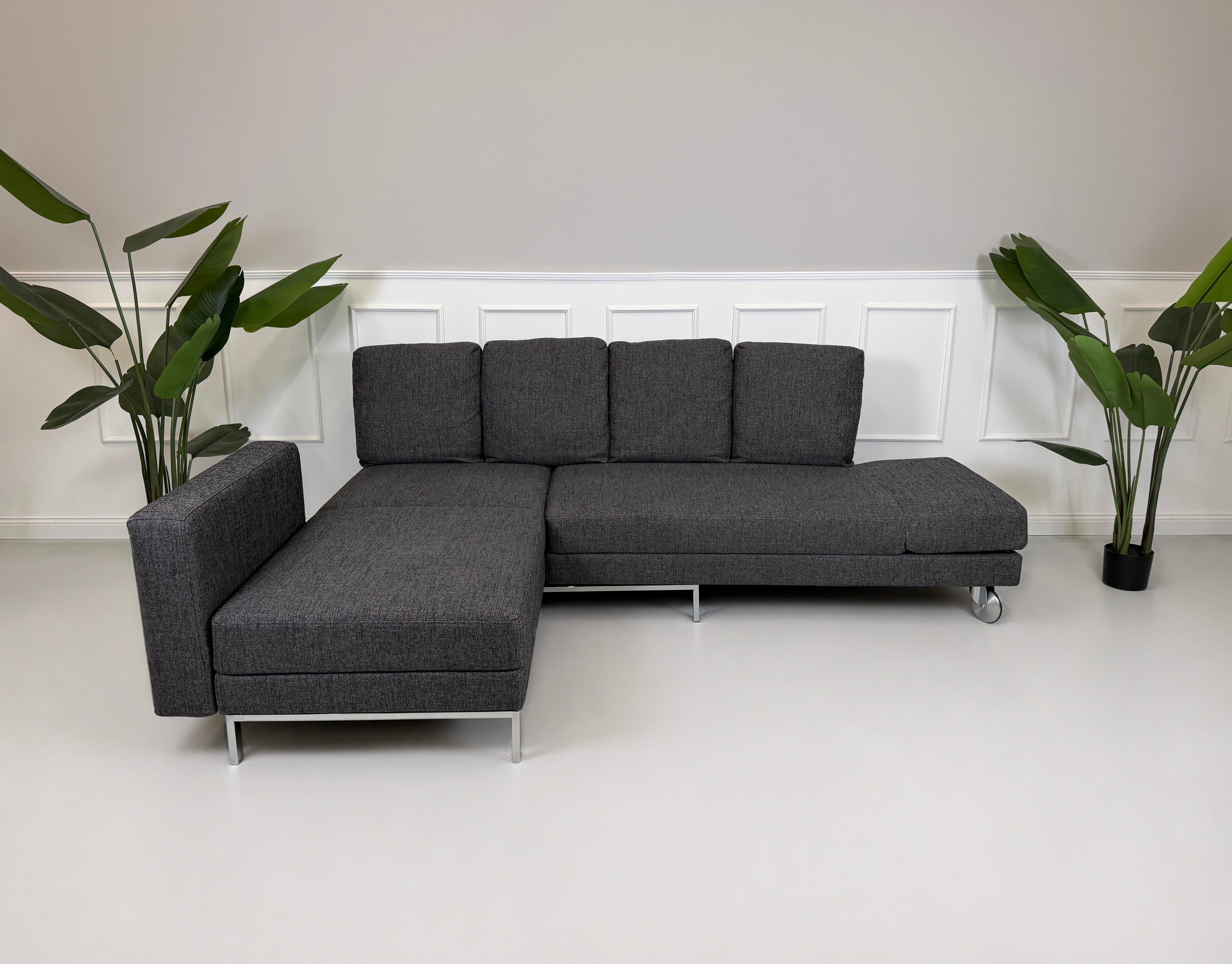 Gebrauchtes graues Brühl Four Two Designer Stoff Sofa vor einer Wand, stilvoll und modern eingerichtet.
