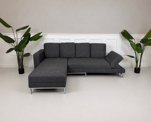 Gebrauchtes graues Brühl Four Two Designer Stoff Sofa vor einer Wand, stilvoll und modern eingerichtet.
